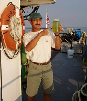 Dr. Bopi Biddanda points to a clear plastic bottle of notably green water.